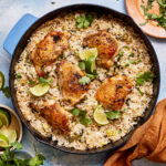A pan of the one pan coconut lime chicken and rice, sitting on a countertop, garnished with cilantro and lime wedges