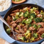 A pan of the quick and easy saucy beef and broccoli, sitting on a countertop with a spoon resting in the pot
