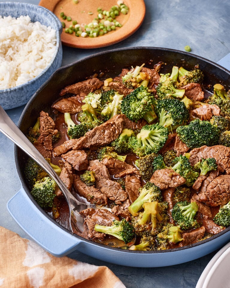 A pan of the quick and easy saucy beef and broccoli, sitting on a countertop with a spoon resting in the pot