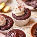 Several ramekins of the easy flourless chocolate cakes, sitting on a countertop, topped with vanilla ice cream and chocolate shavings