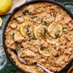 A pan of the creamy lemon chicken orzo, sitting on a countertop with a spoon resting in the pan