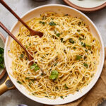 A bowl of the perfect spaghetti aglio e oilio, with a serving fork and spoon sitting inside of the bowl