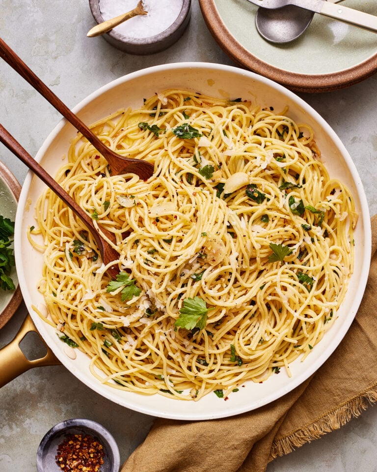 A bowl of the perfect spaghetti aglio e oilio, with a serving fork and spoon sitting inside of the bowl
