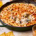 A pan of the creamy spinach artichoke dip, sitting on a countertop with a spoon digging into it