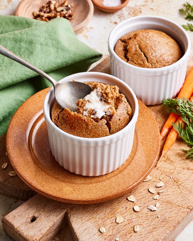 Two ramekins of the single serving carrot cake baked oats, sitting on a countertop with a spoon tucked inside of one of them