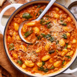 A pot of the italian sausage gnocchi, sitting on a countertop with a ladle placed inside the pan