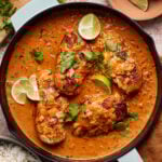A pan of the finished one-pan saucy coconut chicken, sitting on a countertop topped with lime wedges