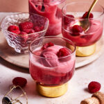 Two of the raspberry sorbet champagne floats, sitting on a countertop topped with fresh raspberries