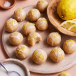A plate full of the no-bake lemon bites, sitting on a countertop next to a bowl of lemons