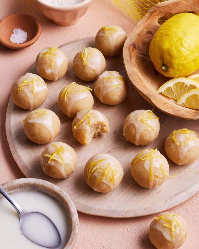 A plate full of the no-bake lemon bites, sitting on a countertop next to a bowl of lemons