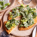 The viral chicken crust caesar salad pizza, sitting on a pizza stone, on a countertop