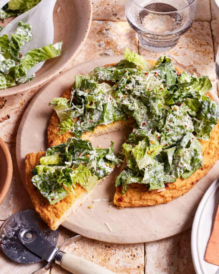 The viral chicken crust caesar salad pizza, sitting on a pizza stone, on a countertop