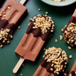 A group of chocolate popsicles with nuts on top.