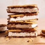 Stacked ice cream sandwiches with chocolate chips and chocolate filling, placed on a parchment sheet against a light background. Crumbs are scattered around.