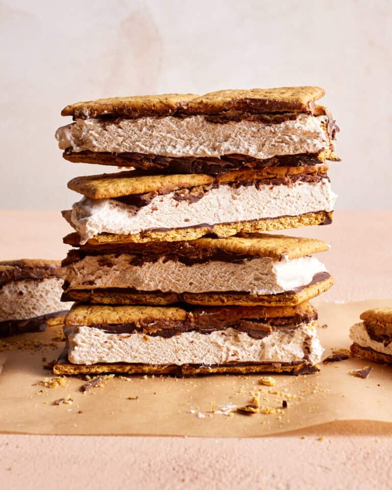 Stacked ice cream sandwiches with chocolate chips and chocolate filling, placed on a parchment sheet against a light background. Crumbs are scattered around.