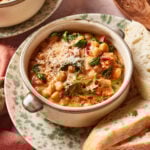A bowl of creamy marry me chickpeas garnished with grated cheese and black pepper, served with slices of crusty bread on a speckled plate.