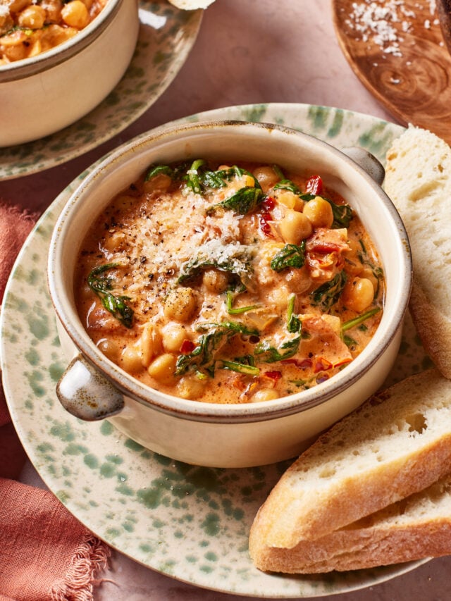 A bowl of creamy marry me chickpeas garnished with grated cheese and black pepper, served with slices of crusty bread on a speckled plate.