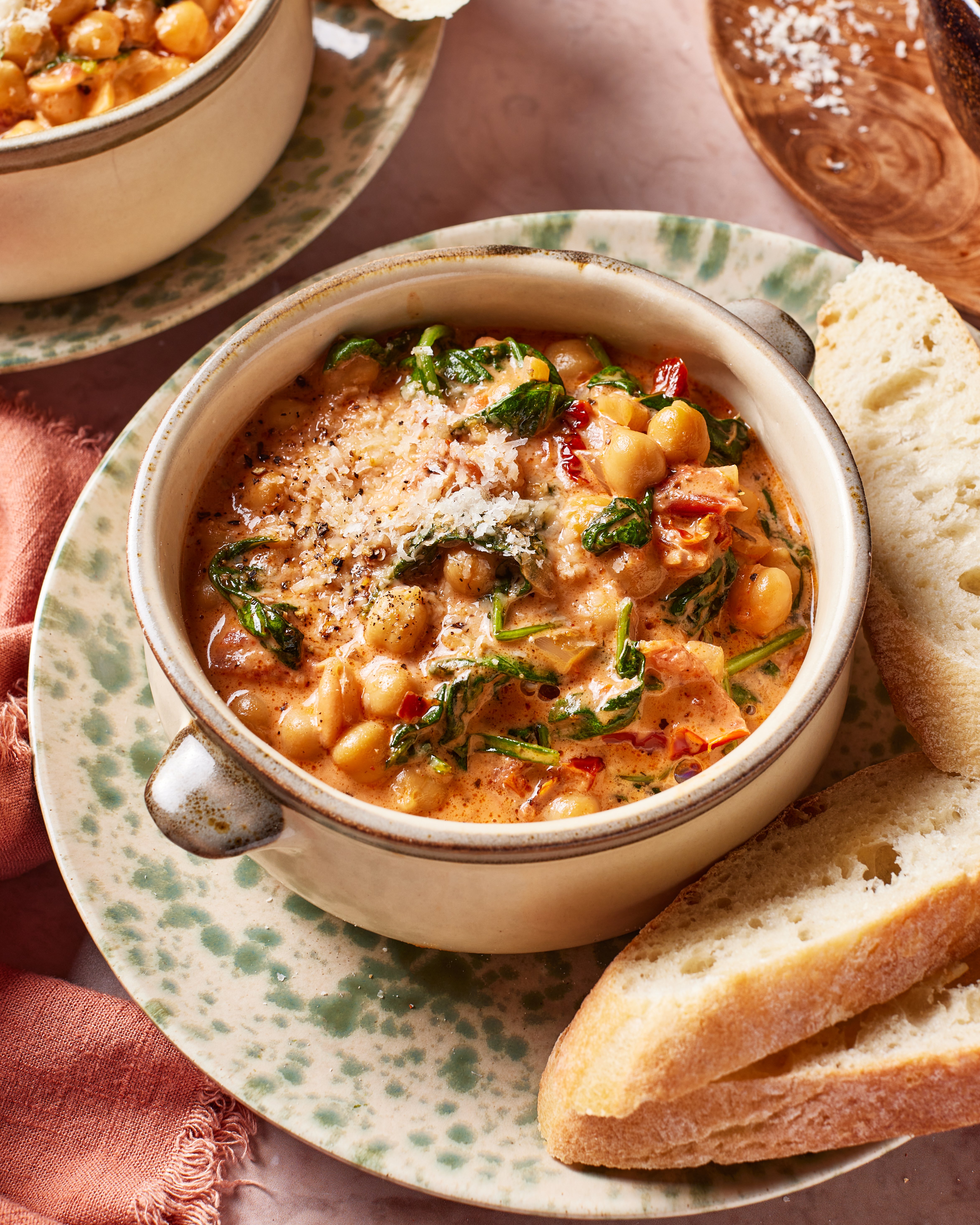 A bowl of creamy marry me chickpeas garnished with grated cheese and black pepper, served with slices of crusty bread on a speckled plate.