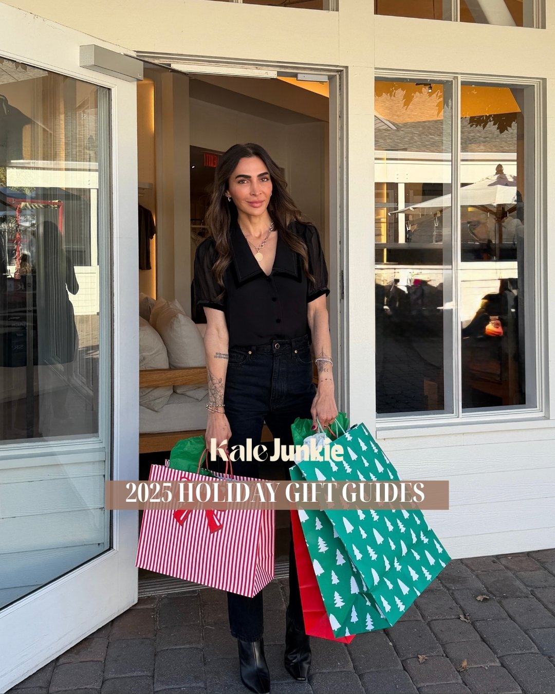 A woman with long dark hair stands outside a store holding several colorful shopping bags. Text on the image reads, "Kale Junkie 2025 Holiday Gift Guides." She is dressed in black and smiling slightly.