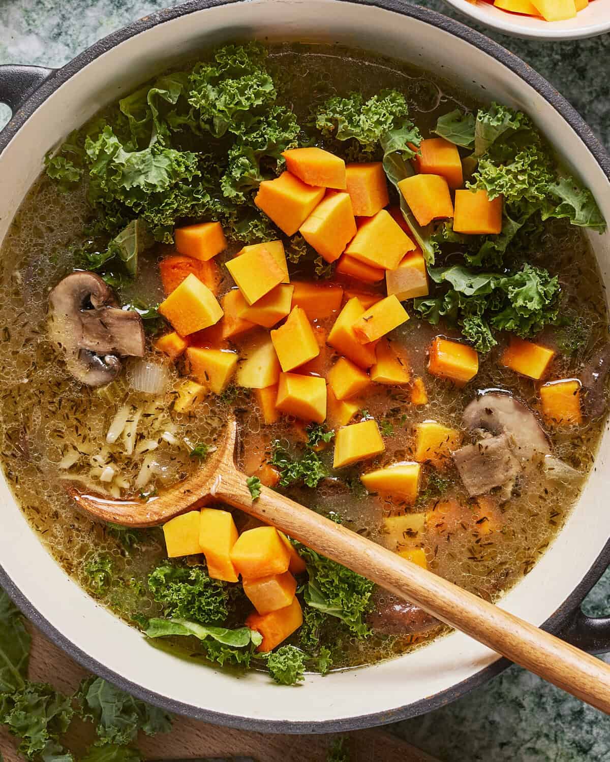 A bowl of soup with vegetables and a wooden spoon.