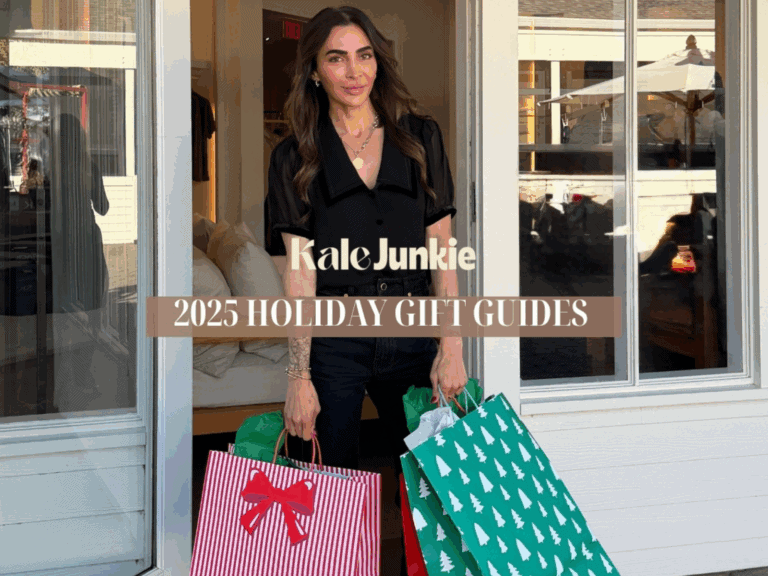 A woman with long dark hair stands in a doorway holding colorful holiday shopping bags. Text reads “Kale Junkie 2025 Holiday Gift Guides.” She is smiling and dressed in black.