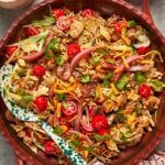A large salad bowl filled with chopped lettuce, cherry tomatoes, shredded cheddar cheese, pickled onions, crispy tortilla strips, fresh cilantro, and grilled chicken, with a serving spoon resting inside.