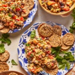 Plates with mixed bean and vegetable salad, round crackers, and fresh herbs on a light surface. Colorful salad contains beans, chopped vegetables, and herbs, served alongside crackers for dipping.