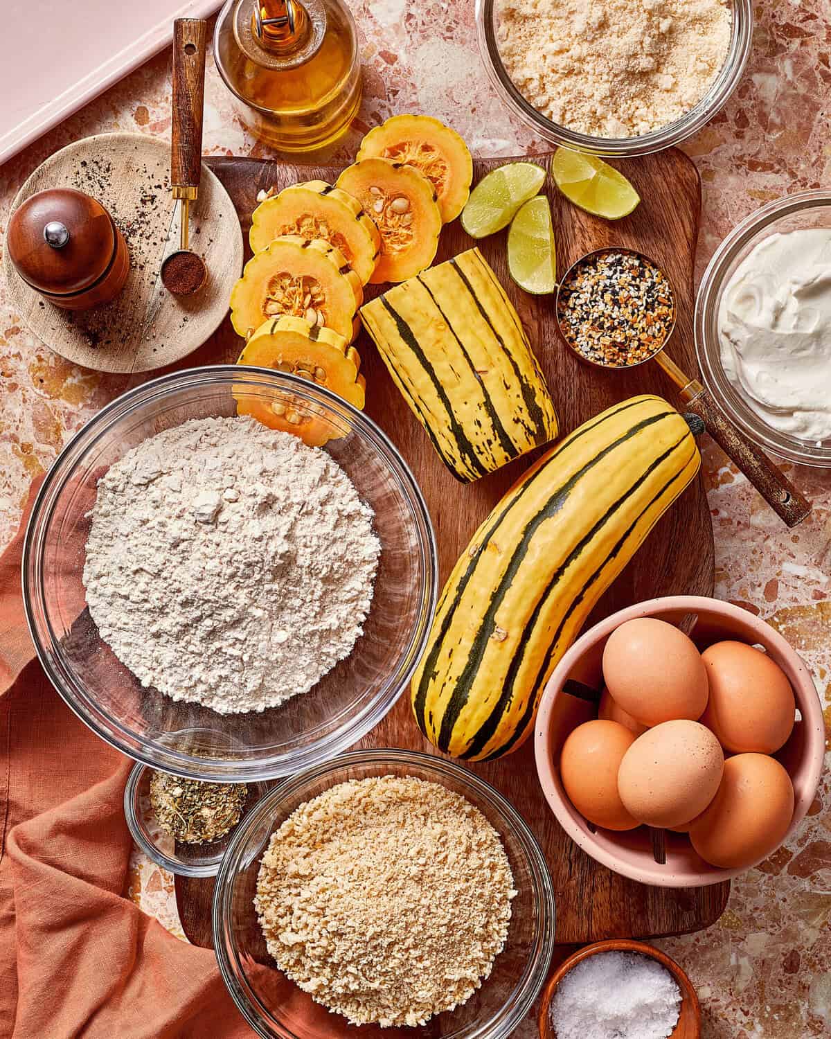 Delicata squash, eggs, flour, breadcrumbs, spices, and other ingredients arranged on a wooden cutting board for cooking.