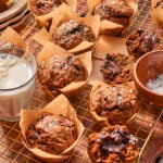 A wire cooling rack filled with chocolate muffins topped with sea salt, including some broken open to reveal melted chocolate centers, next to a glass of milk and a small bowl of salt.
