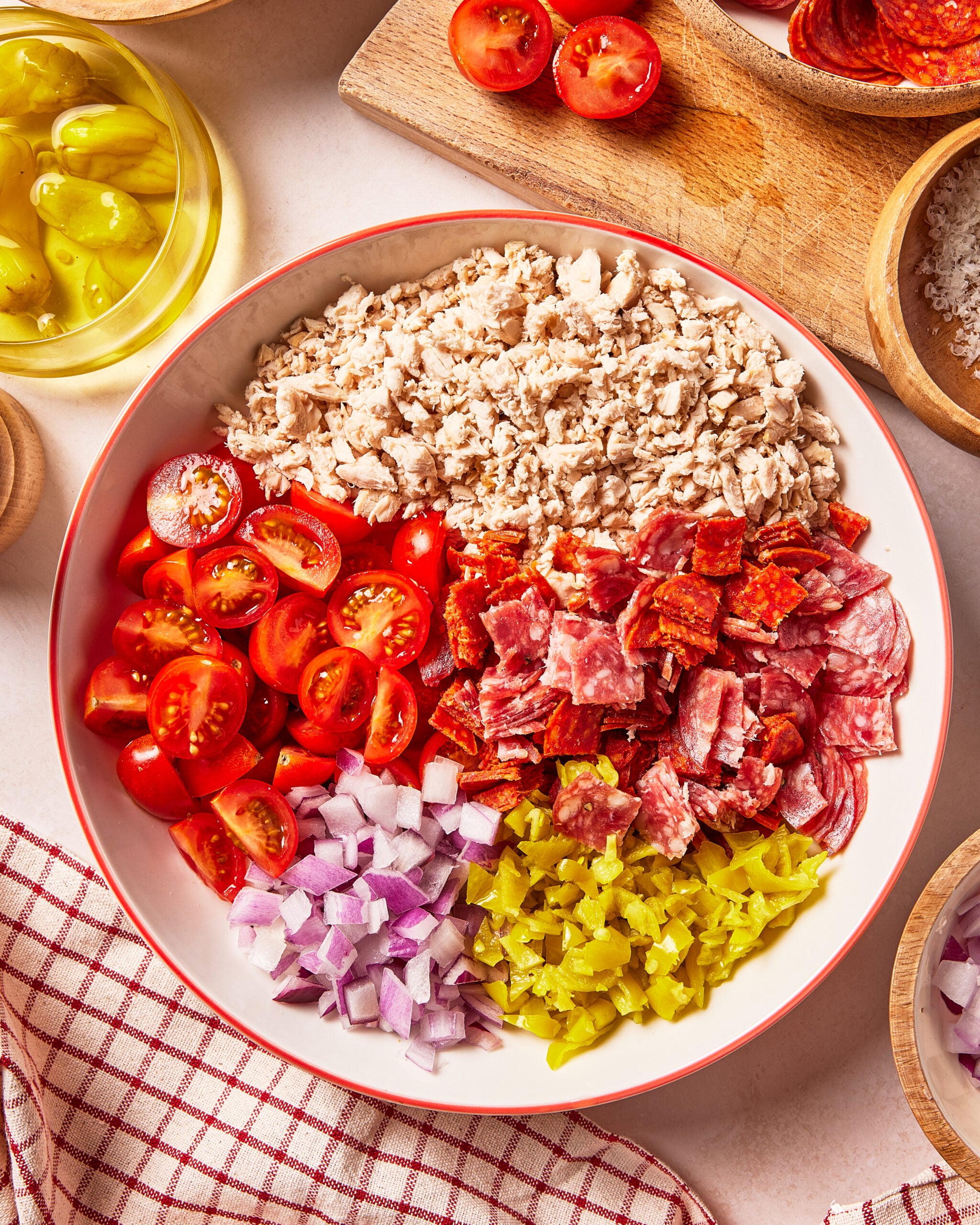 A bowl topped with chopped chicken, diced pepperoni and salami, halved cherry tomatoes, red onion, and banana peppers.