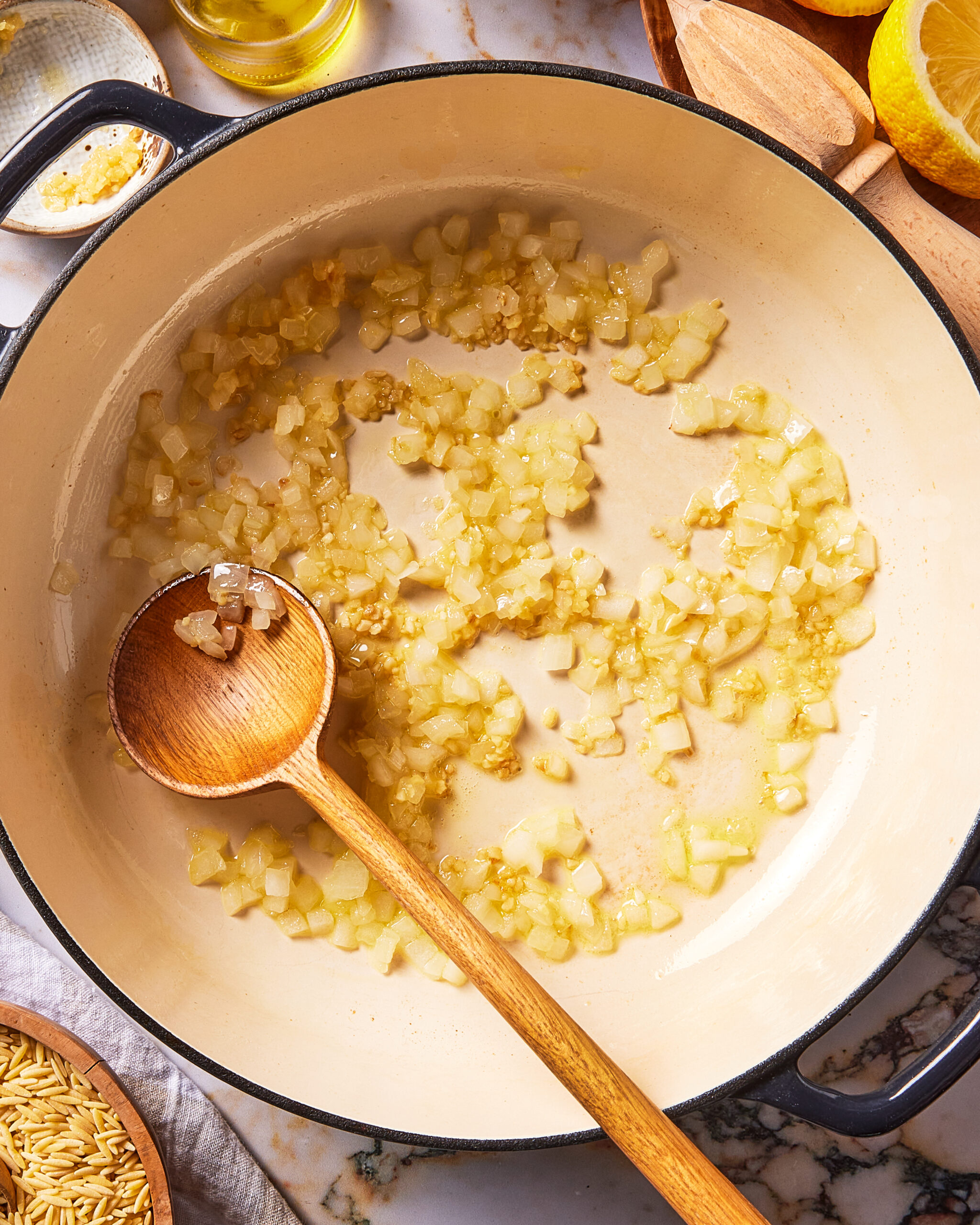 A wooden spoon resting in a Dutch oven filled with sautéing diced onions and minced garlic.