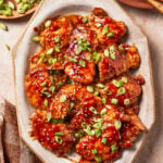 Glazed chicken thighs topped with sesame seeds and sliced green onions on a serving platter.