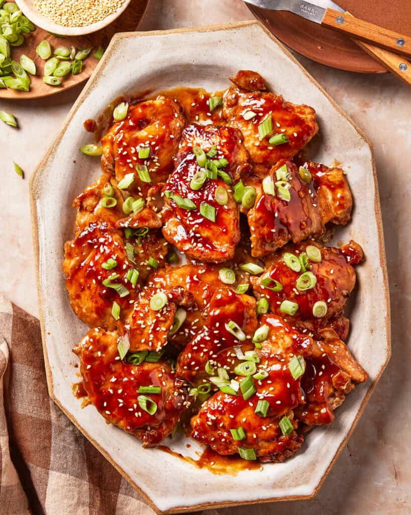 Glazed chicken thighs topped with sesame seeds and sliced green onions on a serving platter.