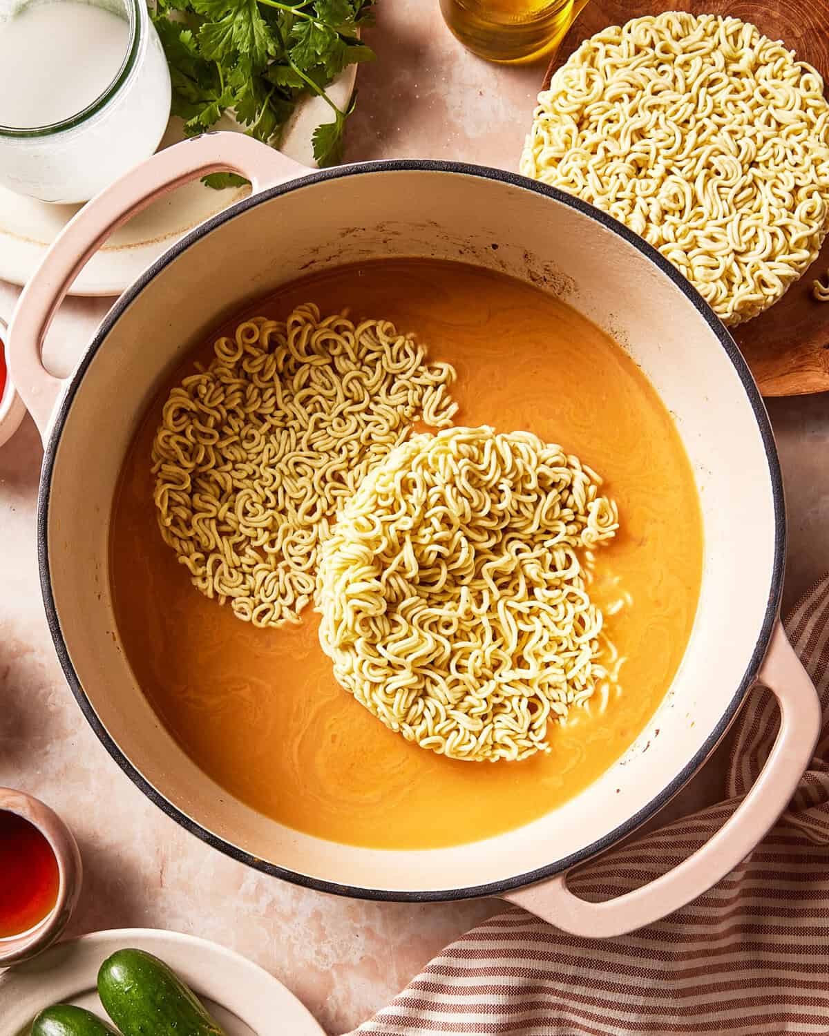 Two dry rounds of instant noodles floating in a pot of orange broth, with an additional round of noodles on the side.