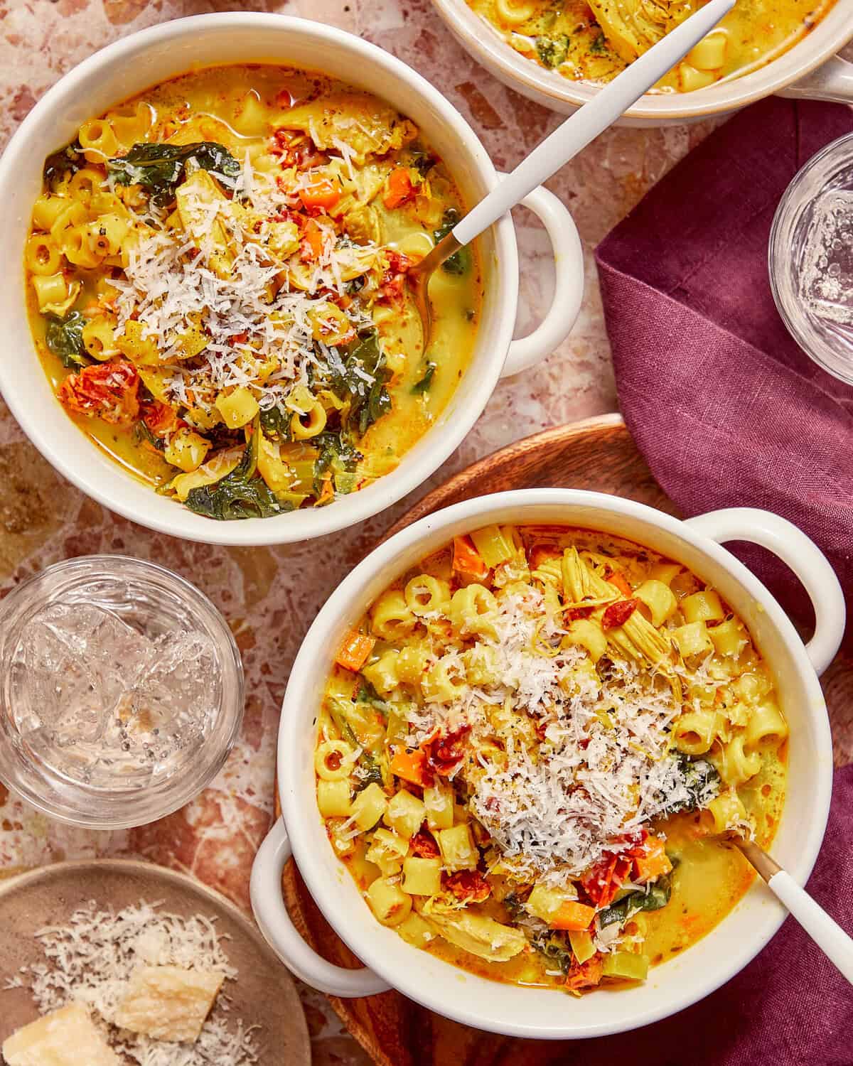 Two bowls of creamy chicken and pasta soup topped with shredded cheese, each served with a spoon.