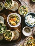 A plate of the spinach feta egg muffins, lined up on top of each other. A small bowl of feta cheese rests to the side