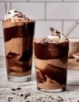 Two glasses of the chocolate cookie milkshake smoothie, in tall glasses topped with whipped cream.