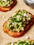 A close-up image of one of the spicy smashed avocado hash brown toasts, placed on a sheet of parchment paper