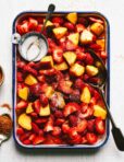 A tray of the sweet & sour tajin peaches & strawberries, sitting on a countertop. A bowl of sugar sits nestled into the peaches and strawberries