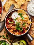 A big bowl of the loaded vegetarian quinoa chili, sitting on a cutting board surrounded by ingredients