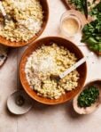 A bowl of the grown-up alphabet pasta, sitting in a bowl on a countertop. A larger bowl of the pasta and a small plate of parsley sits next to the bowl