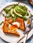 A plate, topped with the grilled cheese egg in a hole, next to an arugula and avocado salad