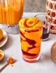 A glass of the copycat Erewhon Turmeric Crush Smoothie, sitting on a countertop surrounded by ingredients needed to make this smoothie