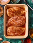 A ceramic tray filled with chicken breasts, topped with the honey mustard chicken marinade