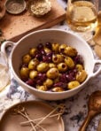 An image of a bowl of the warm marinated olives, sitting on a countertop surrounded by other ingredients in the background