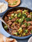 A pan of the quick and easy saucy beef and broccoli, sitting on a countertop with a spoon resting in the pot