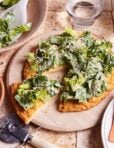The viral chicken crust caesar salad pizza, sitting on a pizza stone, on a countertop