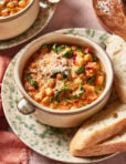 A bowl of creamy marry me chickpeas garnished with grated cheese and black pepper, served with slices of crusty bread on a speckled plate.
