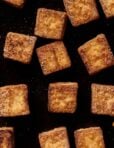 Golden-brown, crispy tofu cubes scattered on a dark surface.
